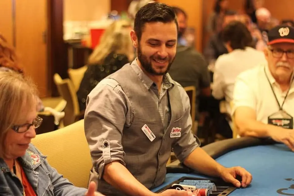 Kristiyan Rukov smiling as he deals cards at a poker table in a casino card room