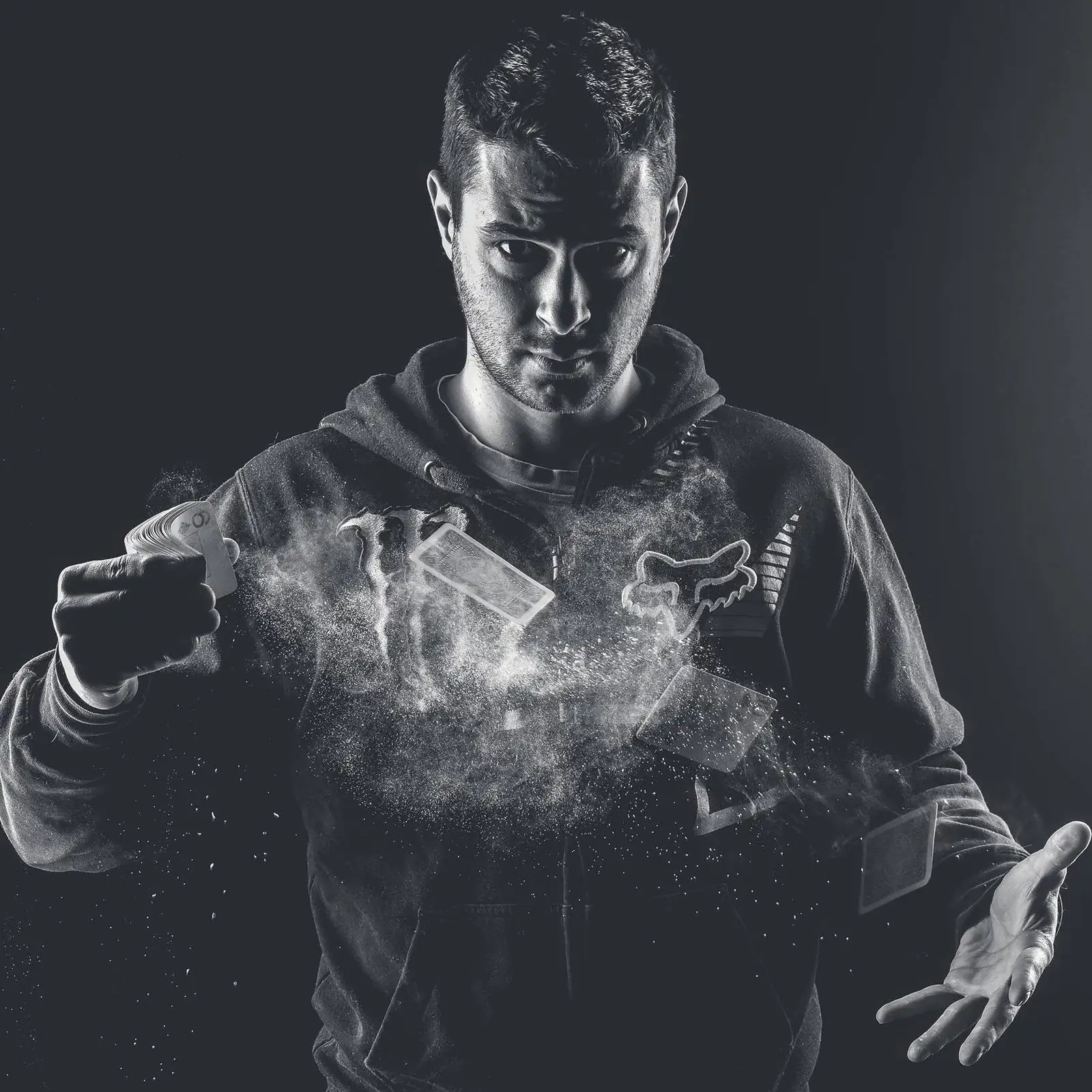 Black-and-white portrait of Kristiyan Rukov throwing playing cards in a cloud of smoke: professional poker player