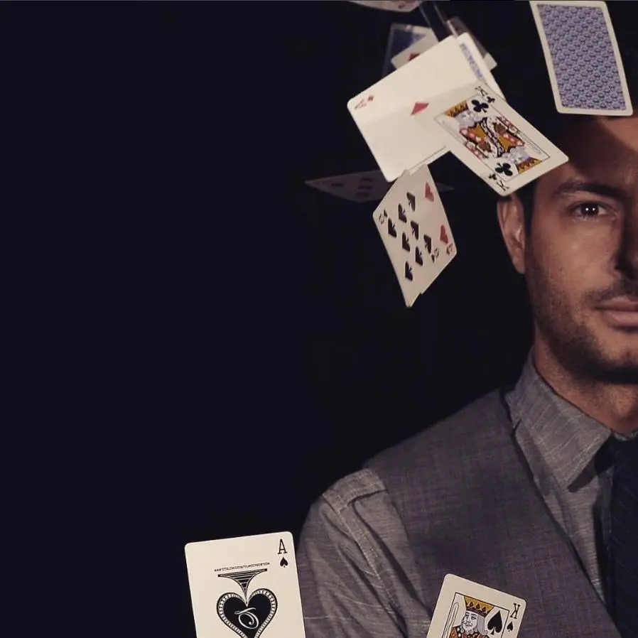 Kristiyan Rukov half in shadow, with playing cards falling around his face